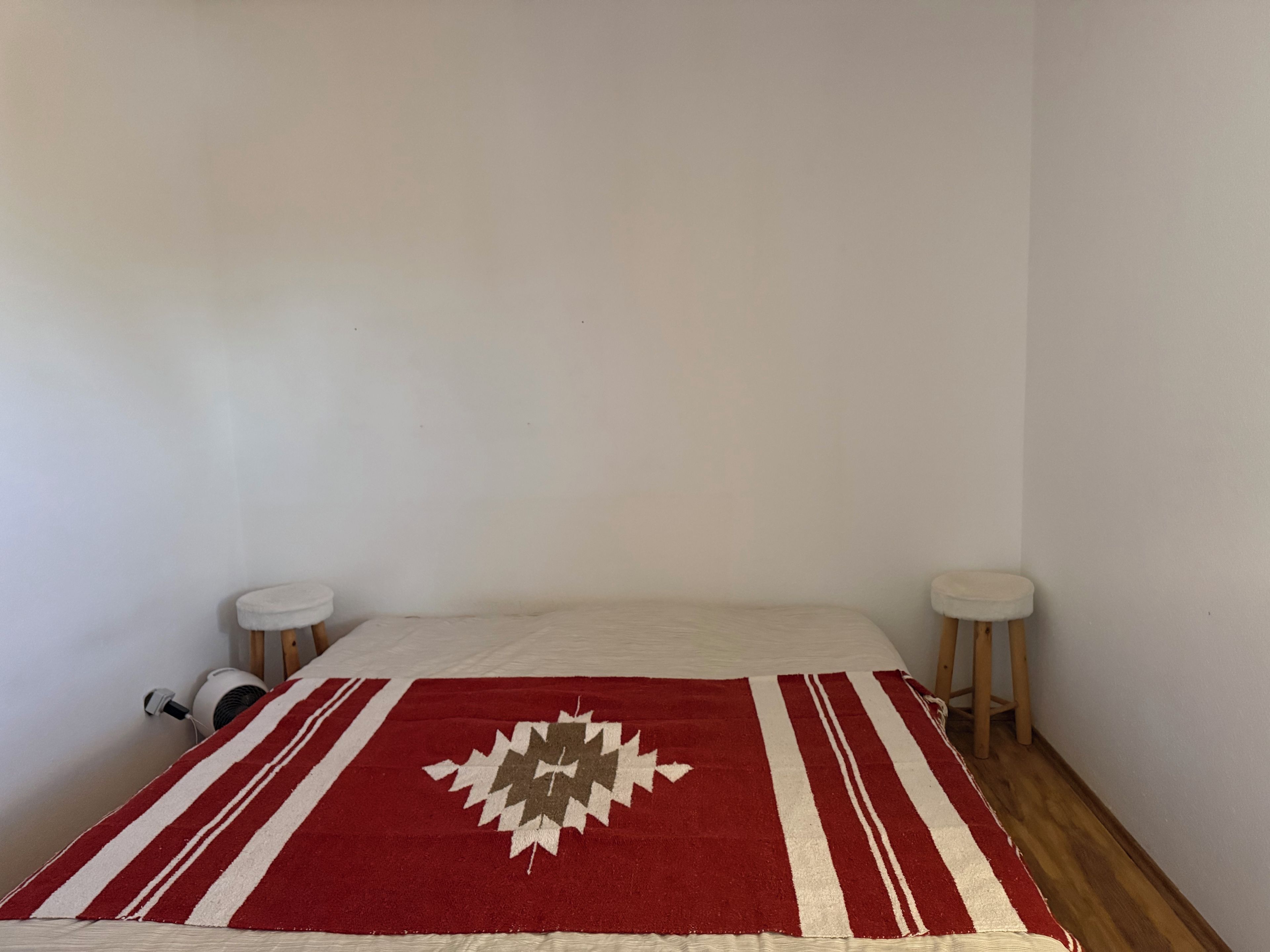 Ein Zimmer mit einem Bett, zwei kleinen Hocker und einer Wandheizung.