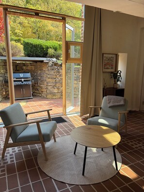 A modern living room with a stone wall, a grill, and a view of a garden. - A little getaway surrounded by nature. (Hüttingen)