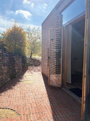 A brick pathway leading to a building with a glass door and a stone wall on one side. - A little getaway surrounded by nature. (Hüttingen)
