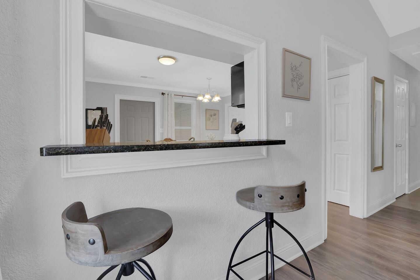 A kitchen with a black countertop, two bar stools, a large mirror, and a ceiling light.