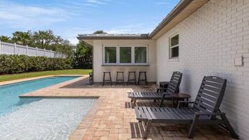 A swimming pool with a patio area, including lounge chairs and a small table.