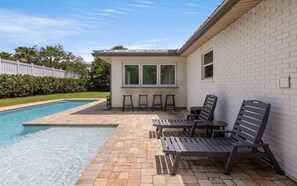 Ein Schwimmbecken mit einer Terrassenanlage, inklusive Liegestühlen und einem kleinen Tisch.