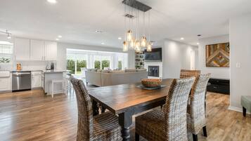 A modern kitchen with white cabinetry, a wooden dining table, wicker chairs, and a hanging light fixture.