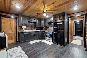 A modern kitchen with dark cabinets, a stainless steel refrigerator, and a built-in oven. - Wood, Water & Wows:Loaded Cabin with GameRoom near Lake (Broken Bow)