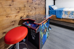 A room with a wooden wall, a bed with blue bedding, and a red stool. - Wood, Water & Wows:Loaded Cabin with GameRoom near Lake (Broken Bow)