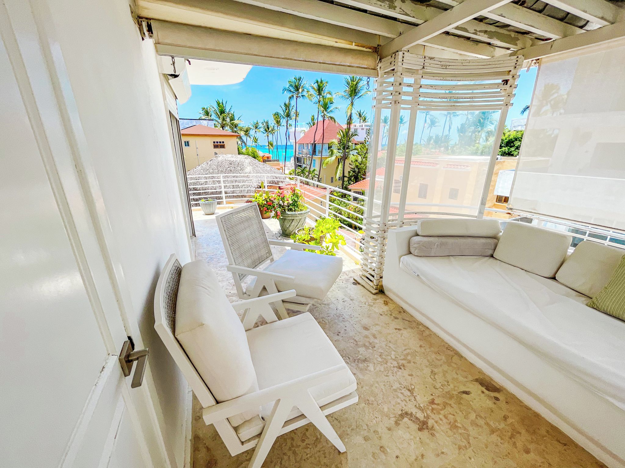 Ein Balkon mit einer weißen Couch und Stühlen, einem kleinen Tisch und Topfpflanzen.