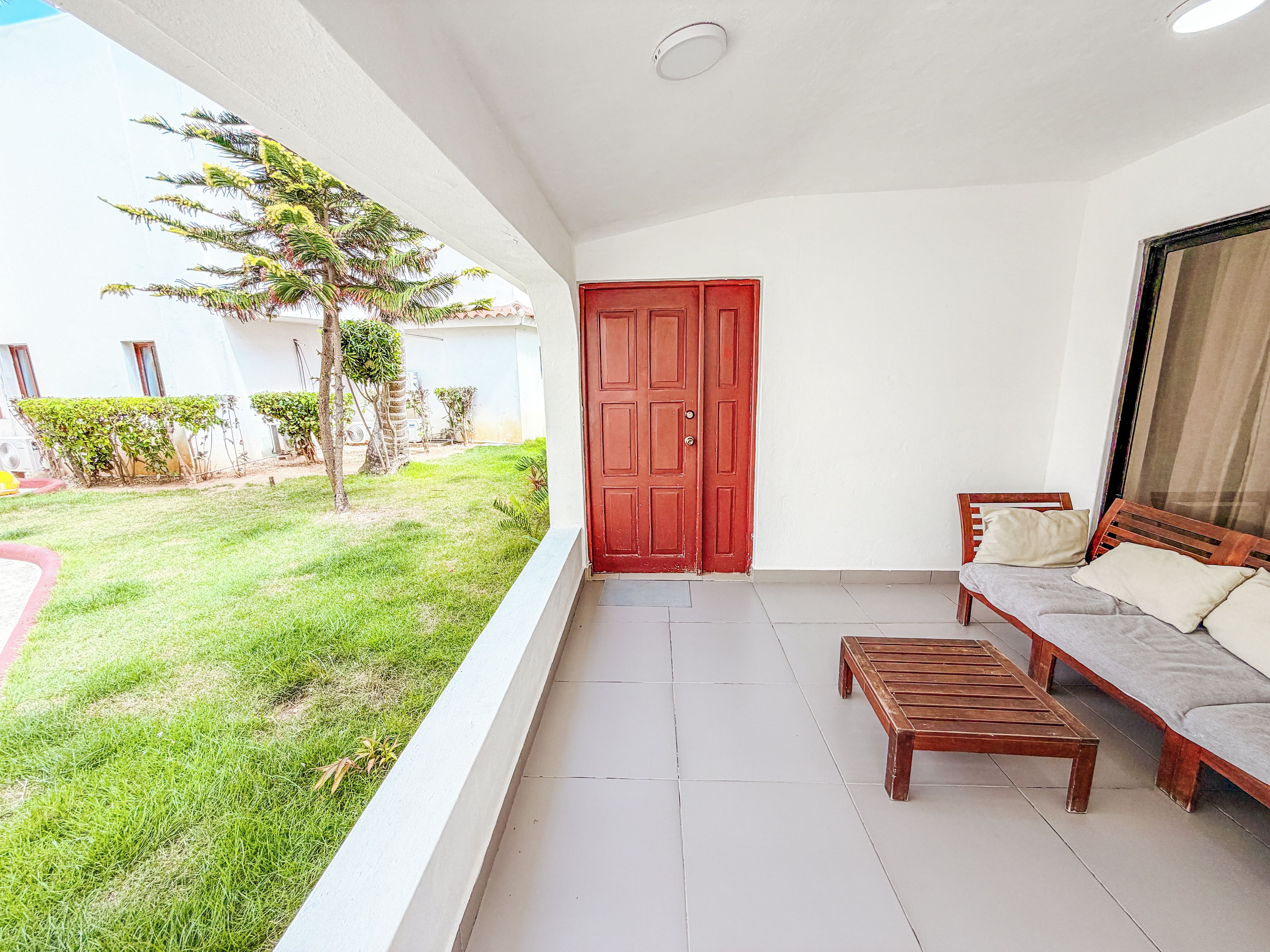 A balcony with a red door, a wooden bench, and a sofa with cushions.