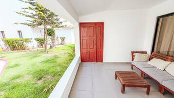 A balcony with a red door, a wooden bench, and a sofa with cushions.