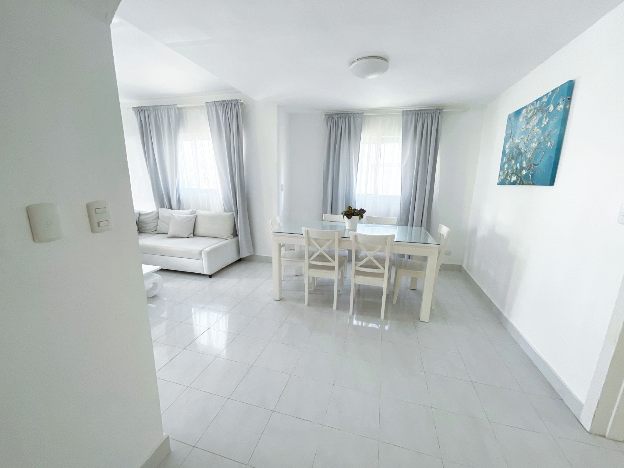 Une pièce lumineuse et blanche, avec une table et des chaises, un canapé et un tableau accroché au mur.