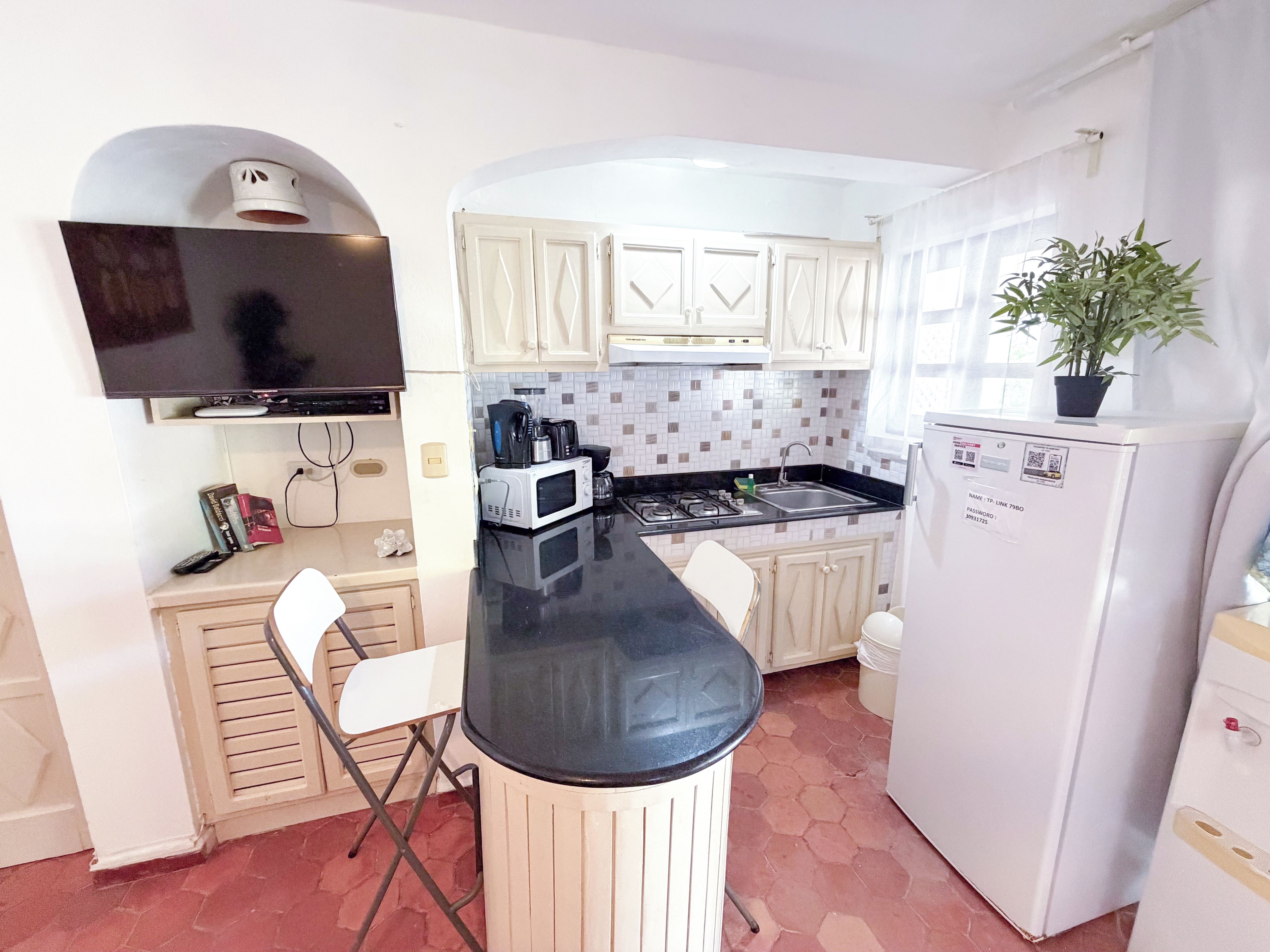 Una cocina compacta con encimera negra, armarios blancos, microondas, estufa y refrigerador.