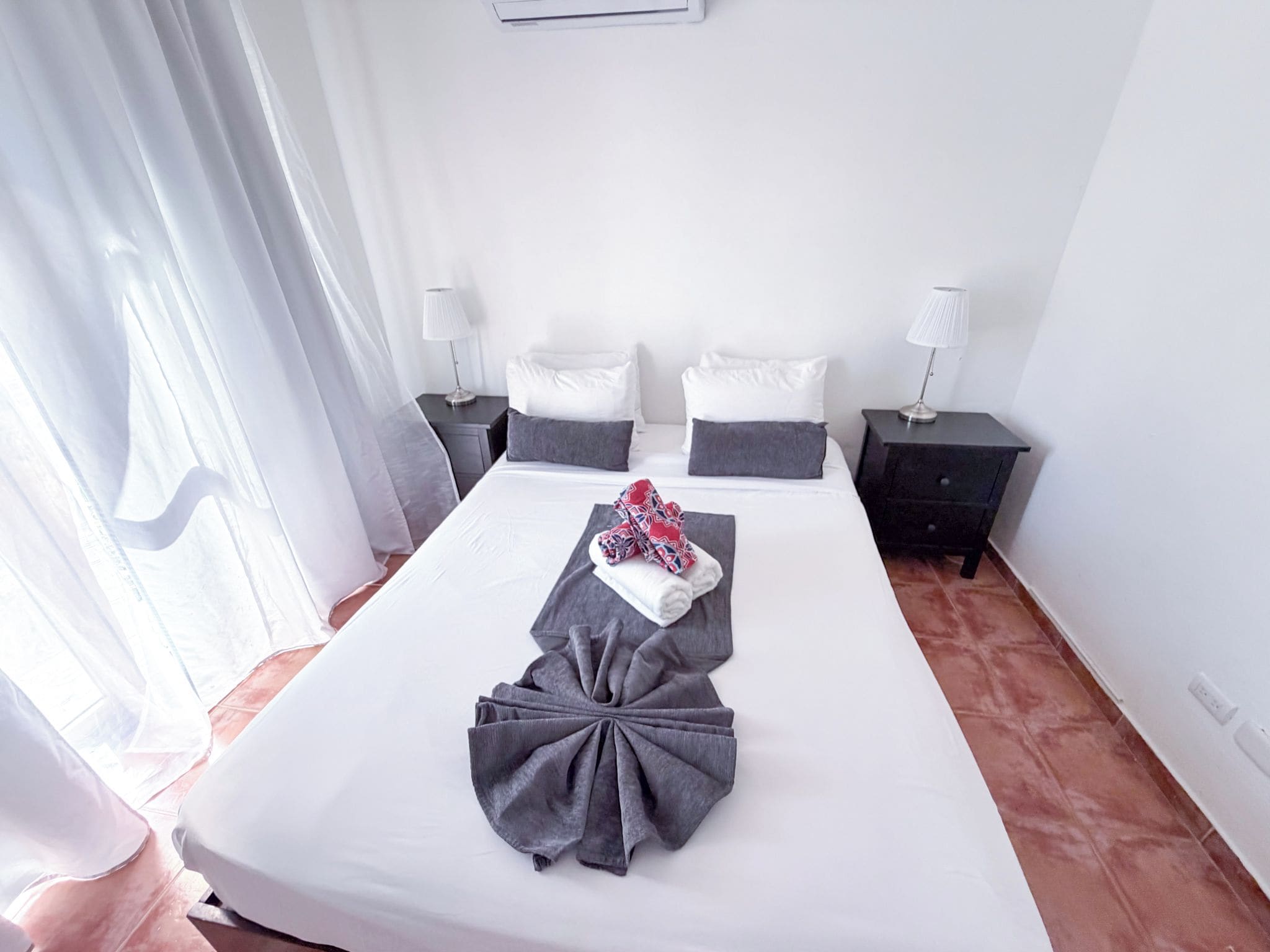 Habitación de hotel con una cama grande, dos mesitas de noche, una lámpara en cada mesita y una ventana con cortinas.