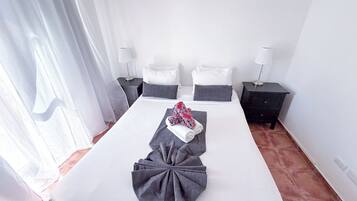 Habitación de hotel con una cama grande, dos mesitas de noche, una lámpara en cada mesita y una ventana con cortinas.