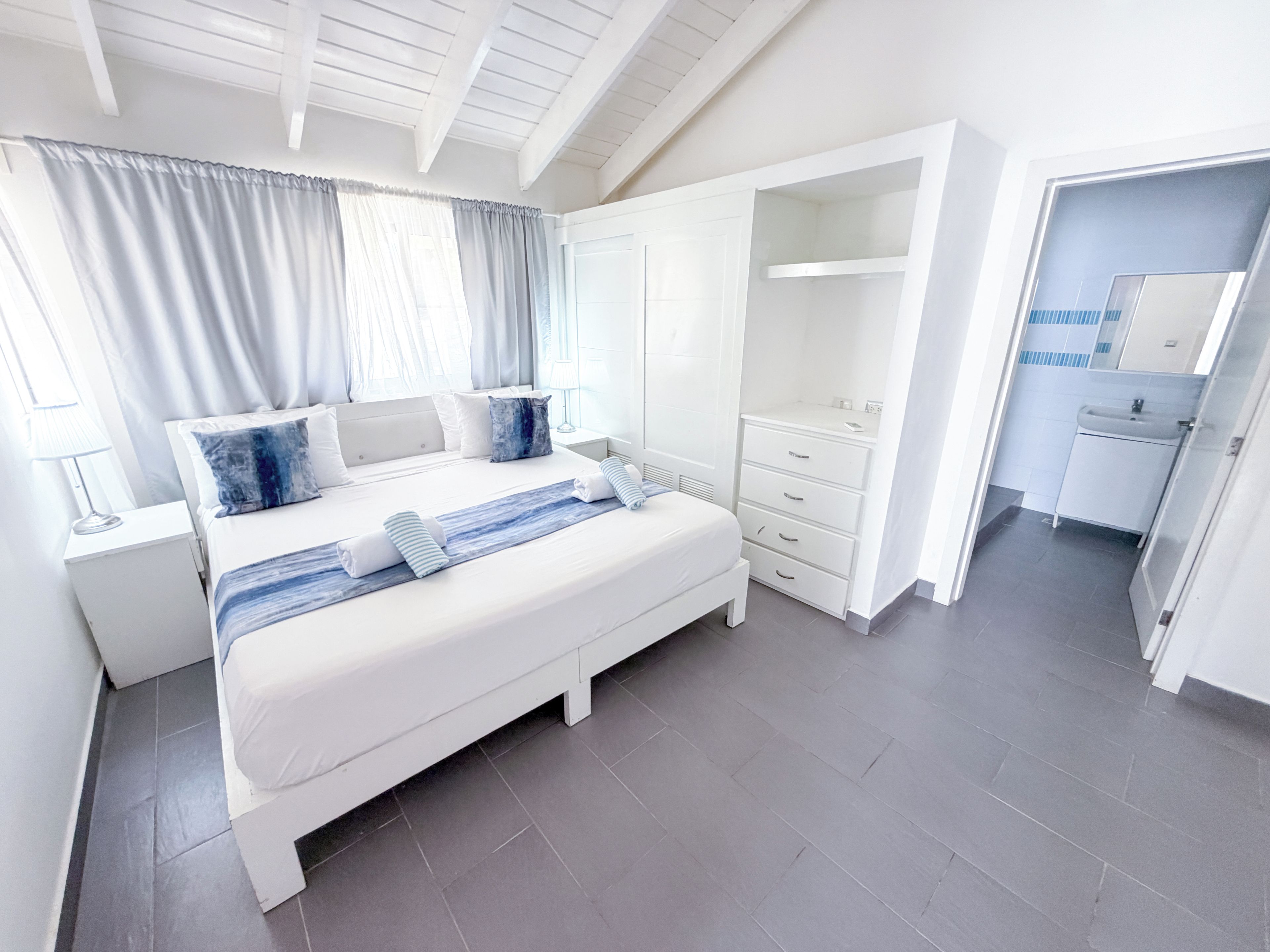 Un dormitorio moderno con una cama grande, mesitas de noche, un armario y un baño con lavabo y espejo.