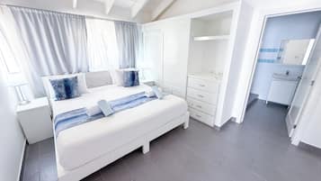 Un dormitorio moderno con una cama grande, mesitas de noche, un armario y un baño con lavabo y espejo.