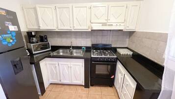 A compact kitchen with white cabinets, a black refrigerator, a microwave, a coffee maker, a gas stove, and a sink.