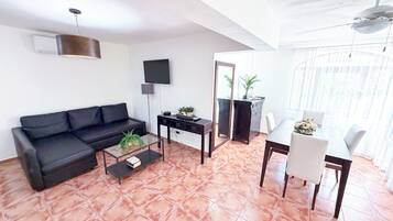 A living room with a sofa, coffee table, TV, and a dining area with a table and chairs.