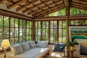 Una habitación con techo de madera, ventanas amplias, una cama con almohadas, una lámpara y un cuadro.
