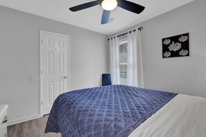 Une chambre à coucher avec un lit, un ventilateur de plafond, une porte et une fenêtre avec des rideaux.