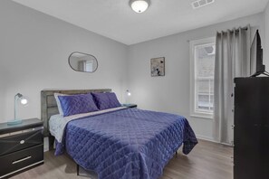 A bedroom with a bed, bedside tables, a mirror, a window with curtains, and a television. - Stylish Duplex! New Remodel! Minutes from Atlanta! - Holiday Home (Norcross)