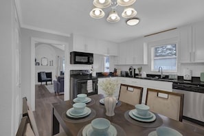 A modern kitchen with white cabinetry, a black microwave, and a dining area with a table set for four. - Stylish Duplex! New Remodel! Minutes from Atlanta! - Holiday Home (Norcross)