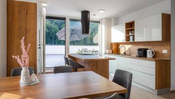 A modern kitchen with a wooden island, white cabinets, and a view of greenery outside.