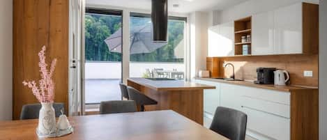 A modern kitchen with a wooden island, white cabinets, and a view of greenery outside.