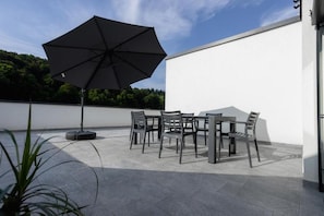 An outdoor patio with a table and chairs, a large umbrella, and a potted plant. - Apartment Dalgona Delux (Podcetrtek)