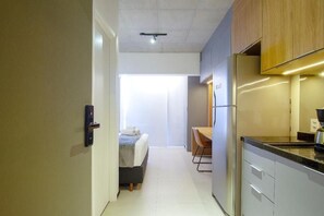 A compact hotel room with a kitchenette, a bed with a white comforter, and a view through a glass door. - On Paulista By Housi (Vila Mariana)