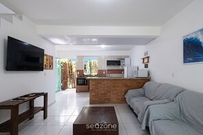 A living room with a grey sofa, a TV mounted on the wall, and a wooden coffee table. - Apt. w/ BBQ in Condo. w/ Pool Ban0004 (Imbituba)