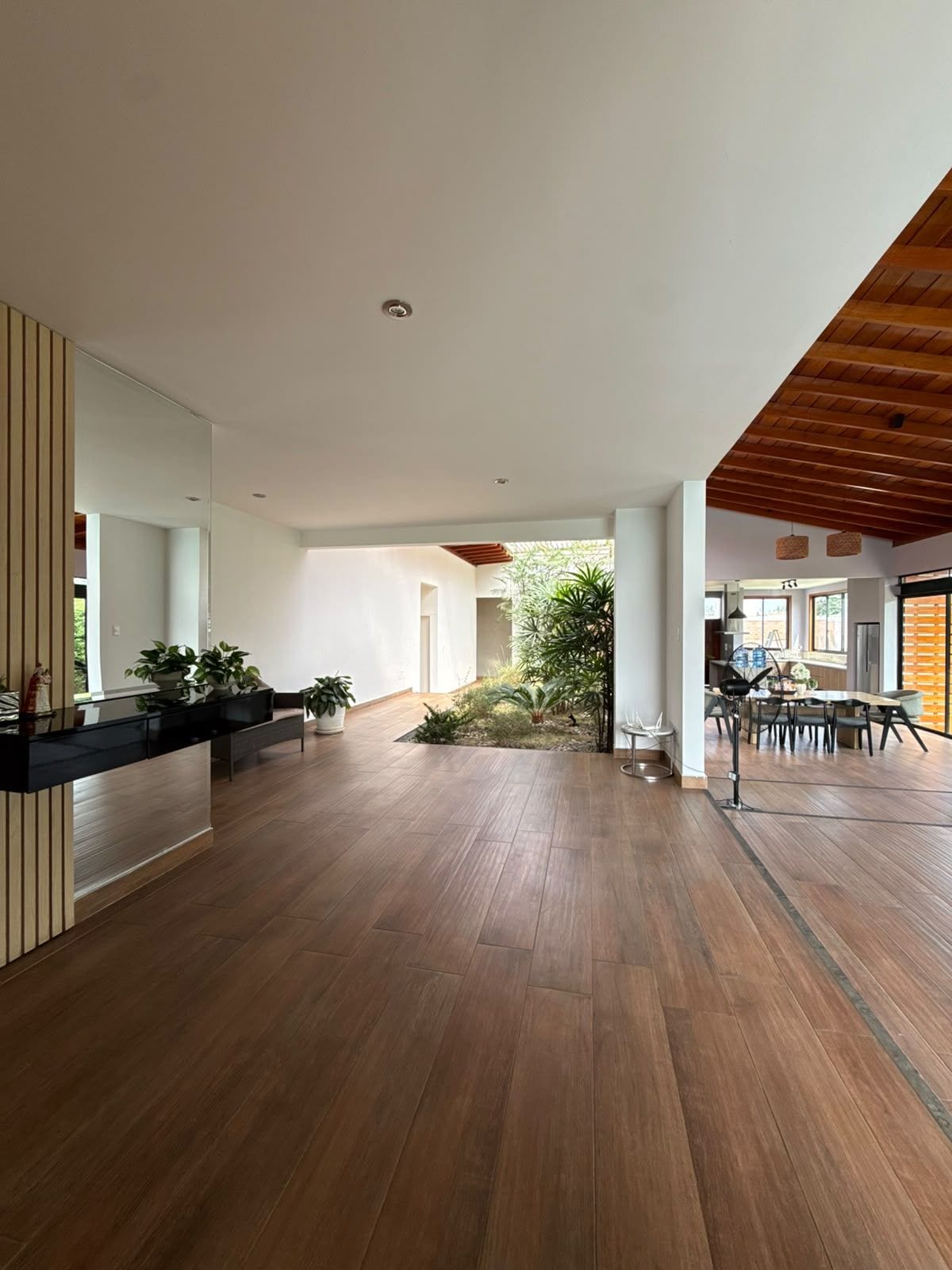 Un interior amplio con suelo de madera, una zona de comedor con mesa y sillas, y un pequeño jardín con plantas.
