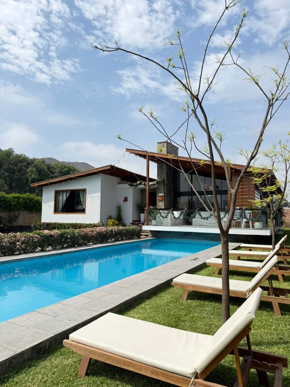 A modern poolside area with lounge chairs, a swimming pool, and a house with a covered patio. - Spacious Home 4BR with Pool in Pachacamac (Lurín)