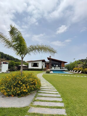 Una casa moderna con piscina, un camino de piedra y un césped cuidado.