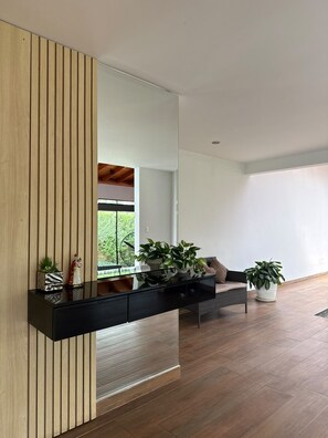 A modern living room with a wooden accent wall, a black console table with plants, a sofa, and a large window. - Spacious Home 4BR with Pool in Pachacamac (Lurín)