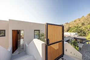 A modern building with a wooden gate, a staircase, and a view of a hillside. - Skypool. Luxury mansion with staff, chef and waiter included. (Ixtapa Zihuatanejo)