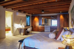 Une chambre avec un grand lit, un bureau et une chaise. Il y a une fenêtre avec des rideaux, un ventilateur de plafond et un téléviseur fixé au mur.