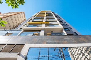 Ein modernes Hochhaus mit Glasfassade, mehreren Balkonen und blauem Himmel im Hintergrund.