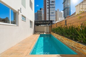 A swimming pool with a wooden deck, surrounded by a white wall and a brick wall with plants. - Apt. w/ Priv. Pool & BBQ Sdm0102 (Balneário Camboriú)