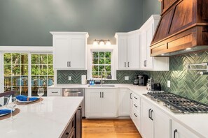 Une cuisine moderne avec des meubles blancs, un dosseret en motif chevrons et un grand îlot central doté d’une plaque de cuisson intégrée.