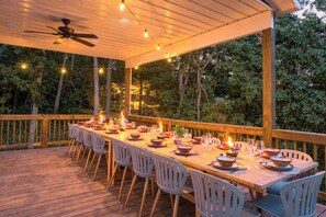 An outdoor dining area with a long wooden table set for a meal, surrounded by chairs, under a covered roof with string lights. - 7 Kings / Hot Tub + Sauna + Game Room / Sleeps 20 (Massanutten)