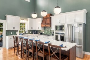A modern kitchen with white cabinets, a stainless steel refrigerator, and a dining area with wooden chairs. - 7 Kings / Hot Tub + Sauna + Game Room / Sleeps 20 (Massanutten)