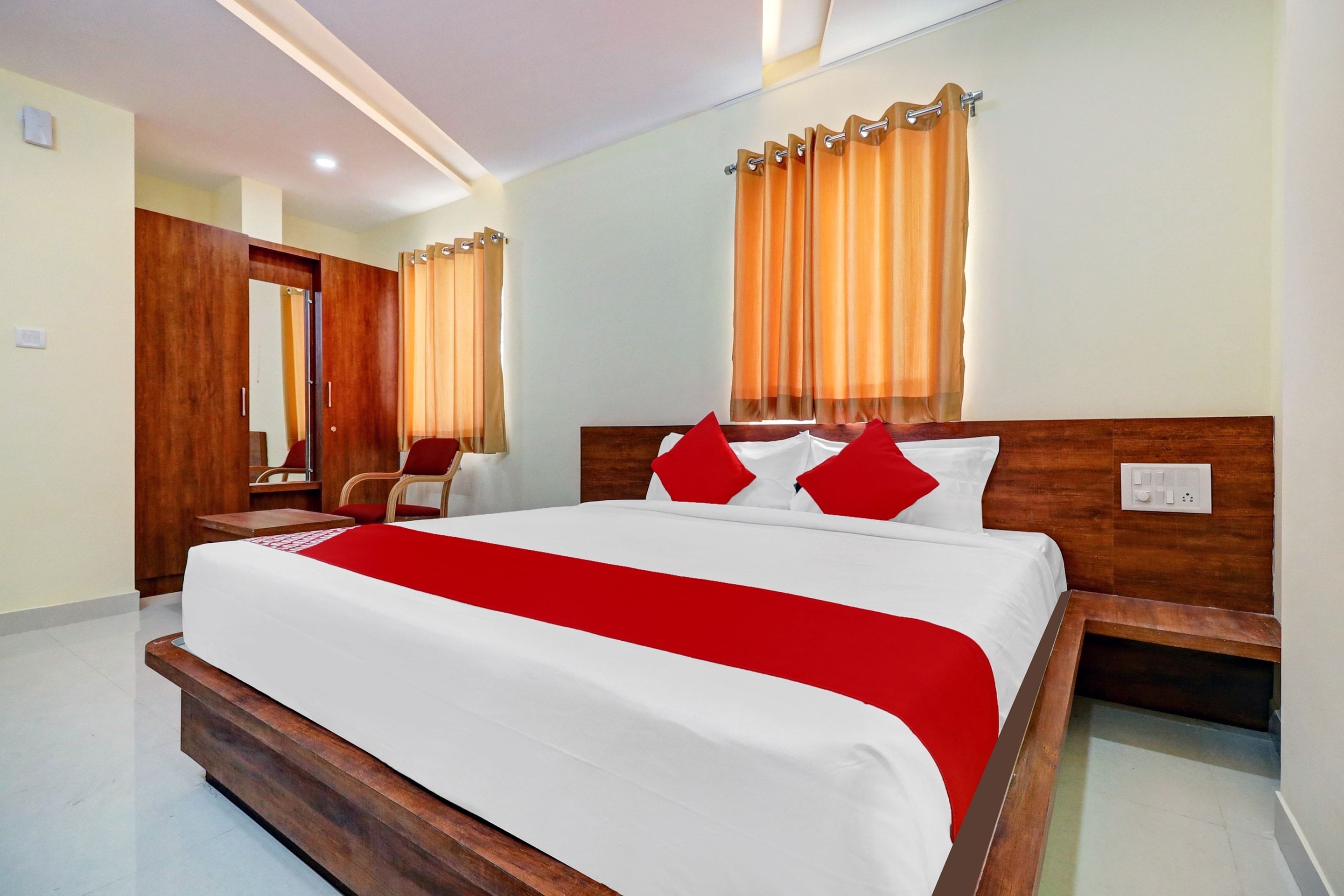 Una habitación de hotel con una cama grande, cabecero de madera y una almohada decorativa roja.