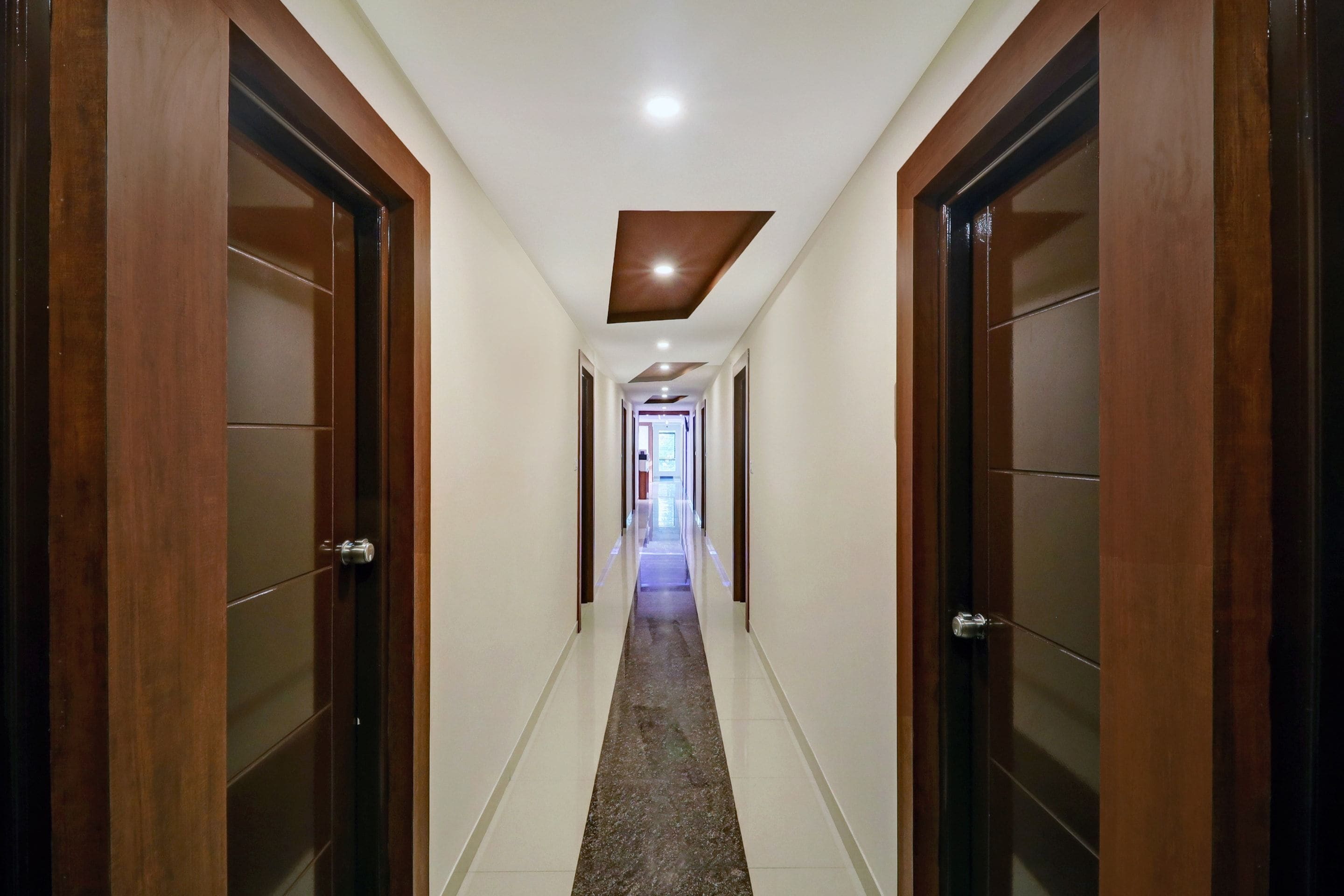 Un pasillo con puertas de madera a ambos lados, que conduce a una habitación luminosa al final.