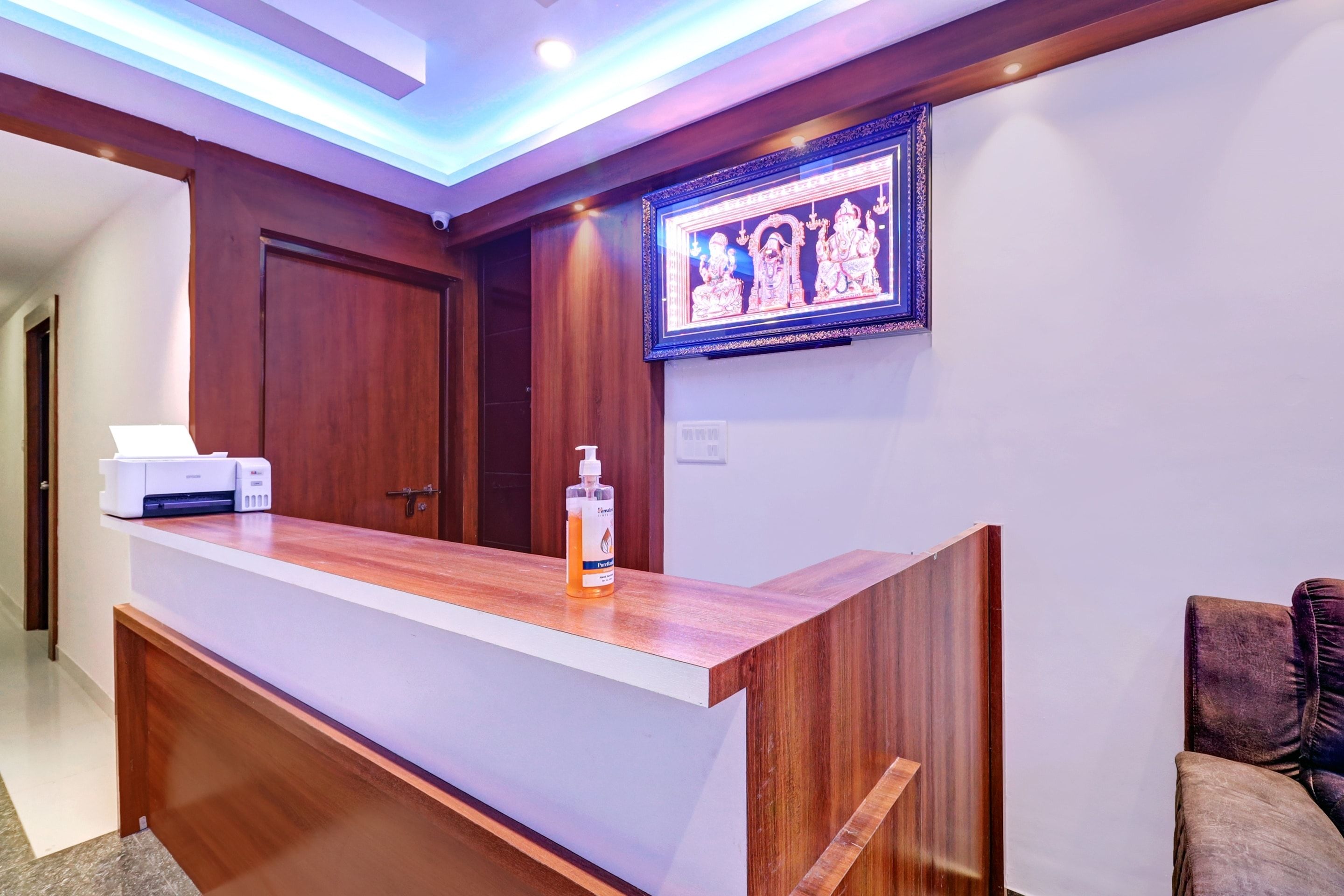A reception desk with a wooden finish, a framed artwork above it, and a bottle of hand sanitizer on the counter.