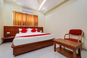 Quarto de hotel com cama de madeira, almofadas vermelhas, mesa de cabeceira de madeira, cadeira vermelha e uma pequena mesa de madeira.