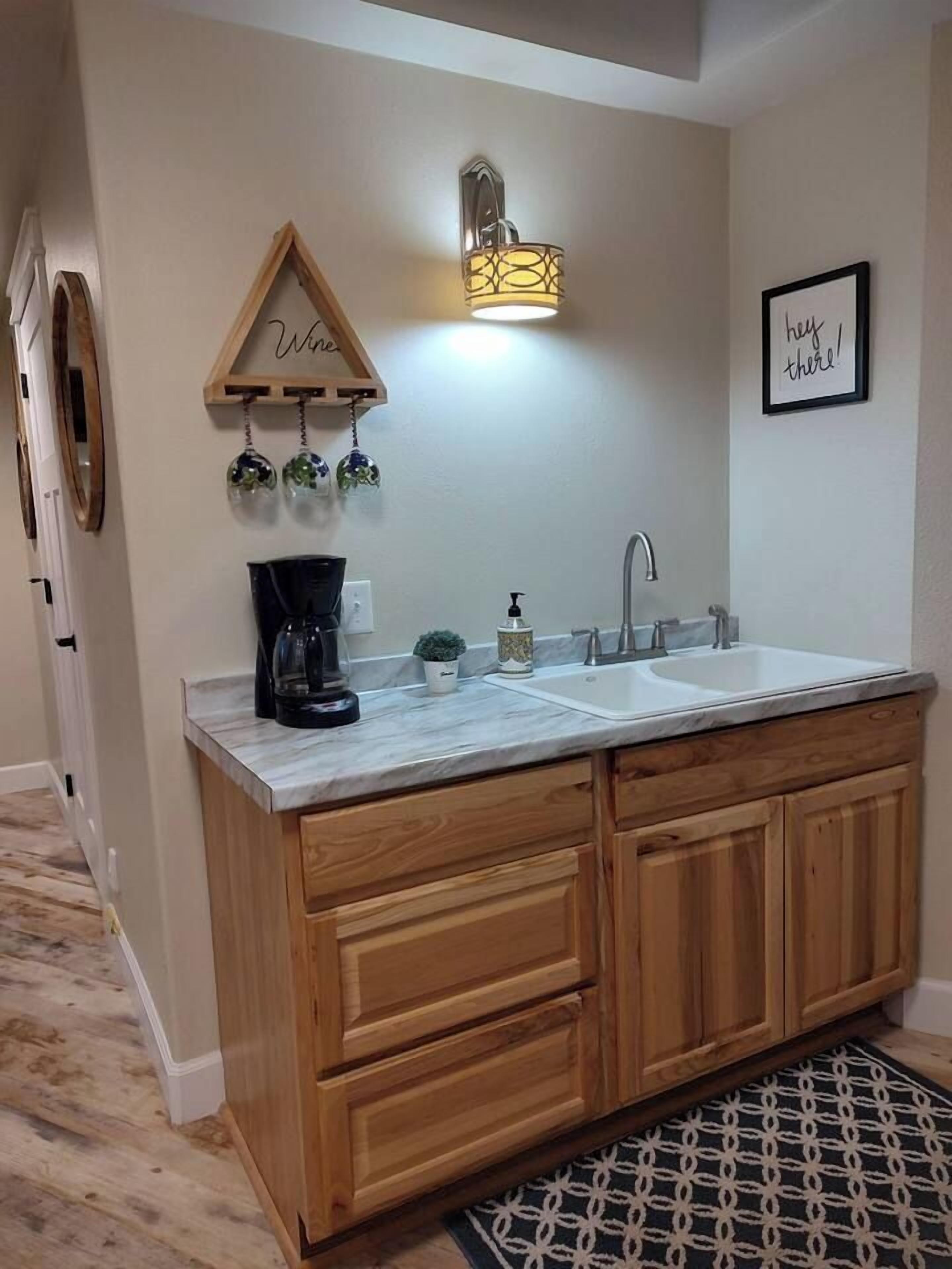 A kitchen with a double sink, wooden cabinets, a coffee maker, and a wall-mounted light fixture.