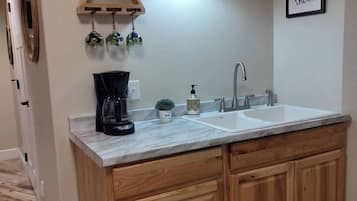 A kitchen with a double sink, wooden cabinets, a coffee maker, and a wall-mounted light fixture.