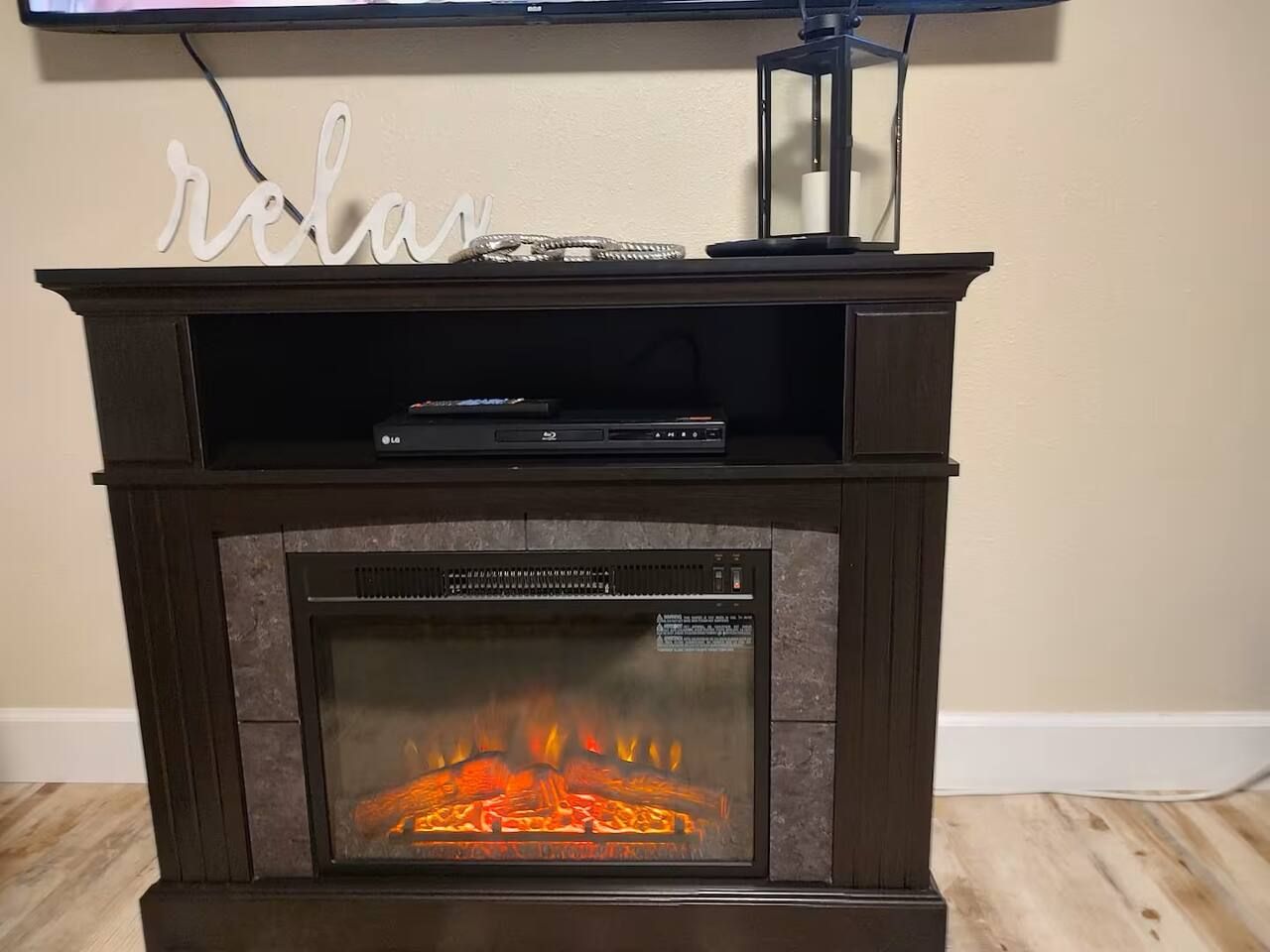 A fireplace with a TV on top, a decorative sign above it, and a remote control on the mantel.