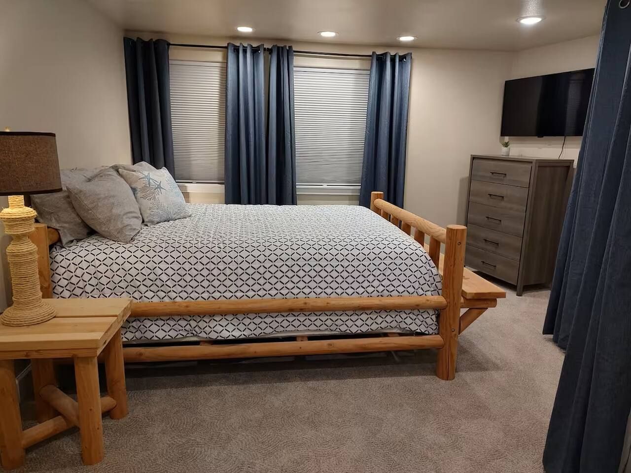 Quarto com cama, mesas de cabeceira, cômoda e televisão fixada na parede.