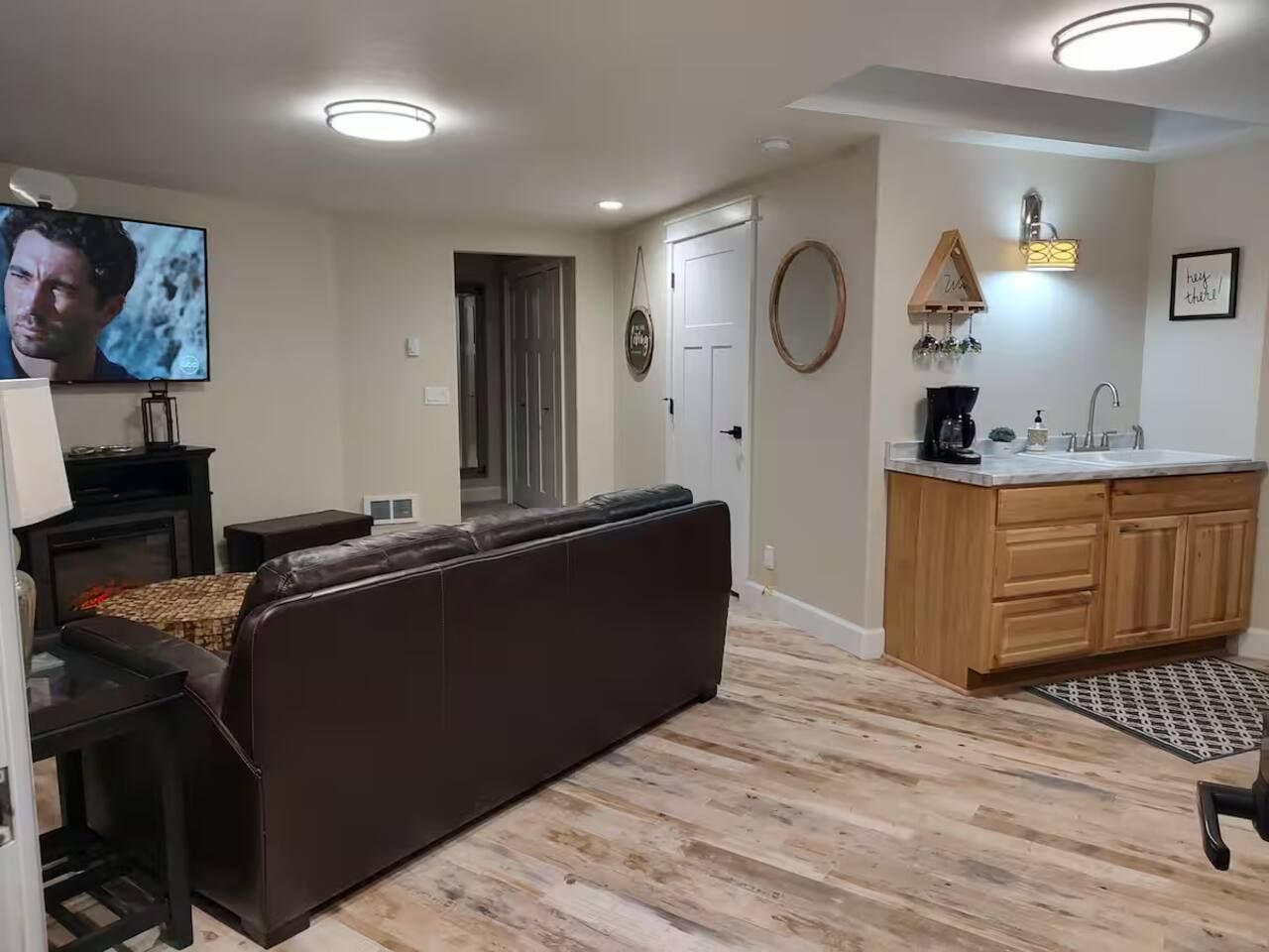 Sala de estar com sofá, televisão, lareira e área de cozinha com armários de madeira e pia.