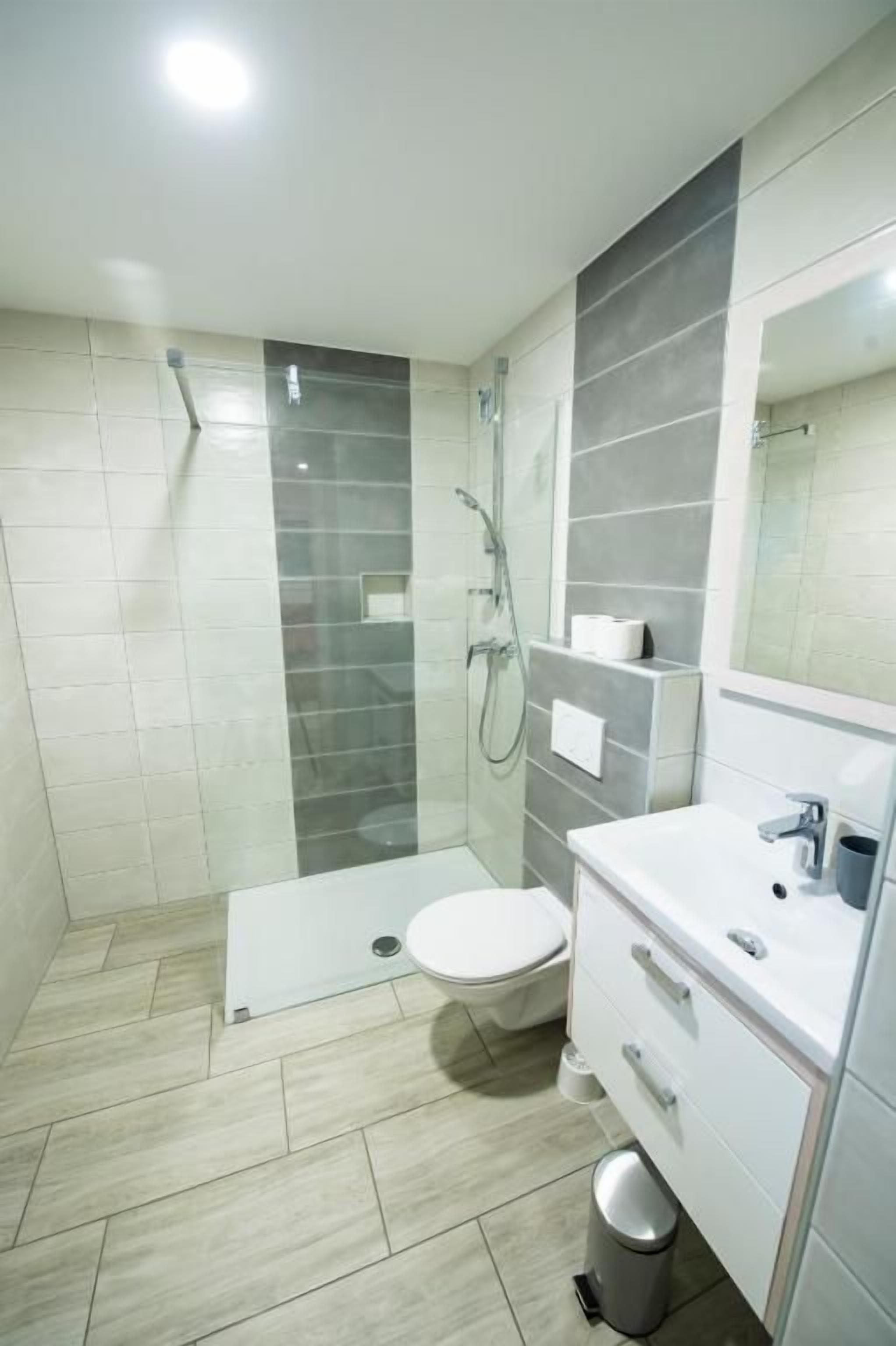 Een moderne badkamer met een douchecabine van glas, een toilet en een wastafel met spiegel.